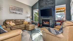 A modern living room with a leather sofa set, a fireplace, and a large flat-screen TV mounted on the wall. - Spacious Modern Gorgeous Mountain Views Fort Carson Fire Pit!  (Colorado Springs)