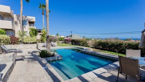 Una piscina con bordo in pietra, circondata da palme e siepi, con vista su un edificio sullo sfondo.