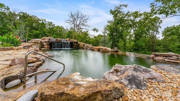 A natural pool with a waterfall, surrounded by rocks and trees.