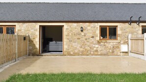 A stone building with a tiled roof, a wooden fence, and a concrete patio.