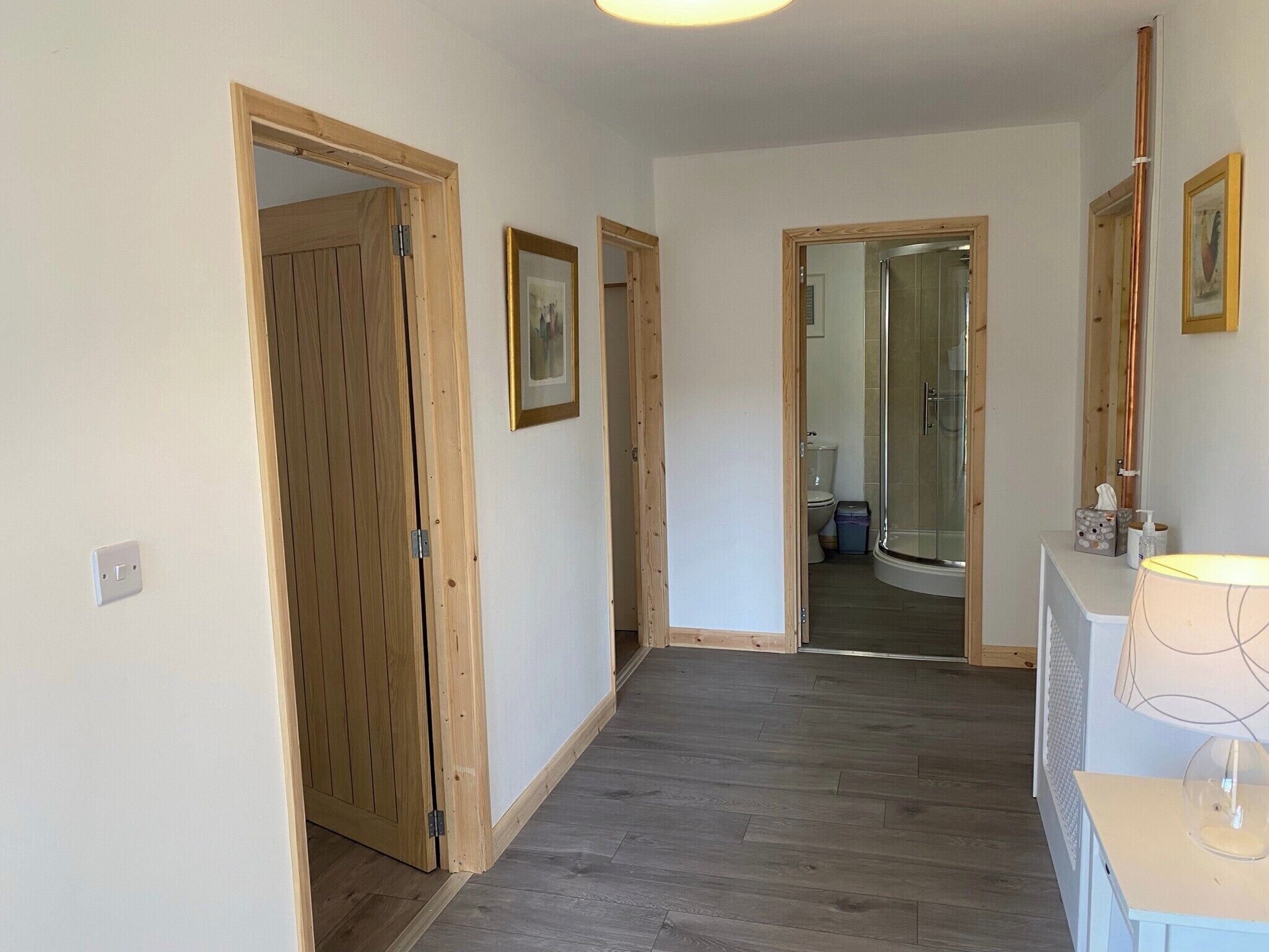 A hallway with wooden doors, a framed picture on the wall, and a bathroom visible through an open door.