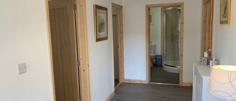 A hallway with wooden doors, a framed picture on the wall, and a bathroom visible through an open door.