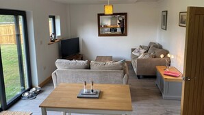 Een moderne woonkamer met een bank, een houten tafel en een televisie. Er is een schuifdeur naar een balkon.