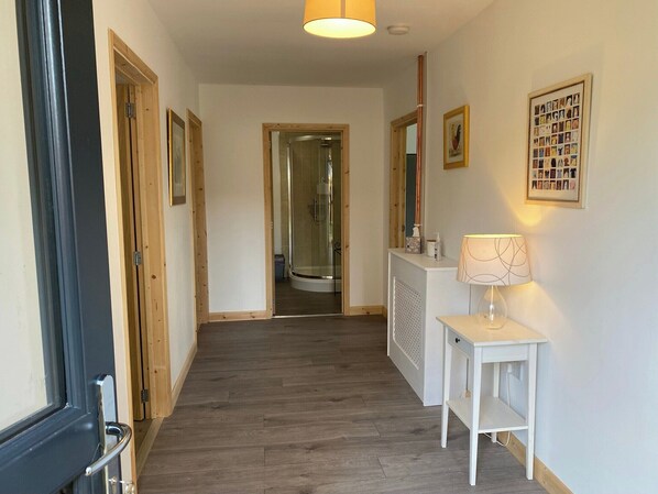Un couloir avec un plancher en bois, un mur blanc et une porte sur le côté gauche.