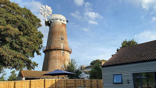 Een achtertuin met een windmolen, een houten omheining, een tafel met stoelen en een huis met een glazen deur.