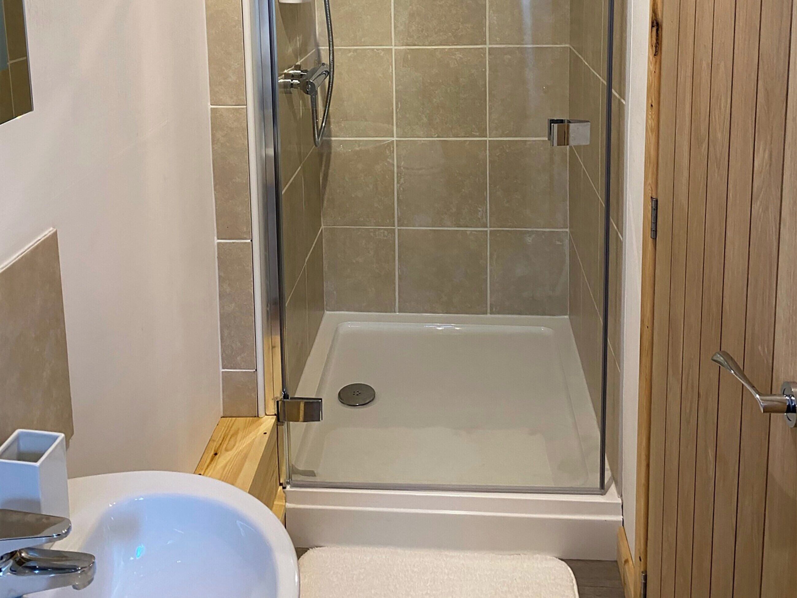 Una dutxa amb porta de vidre, un lavabo blanc i un terra de fusta.