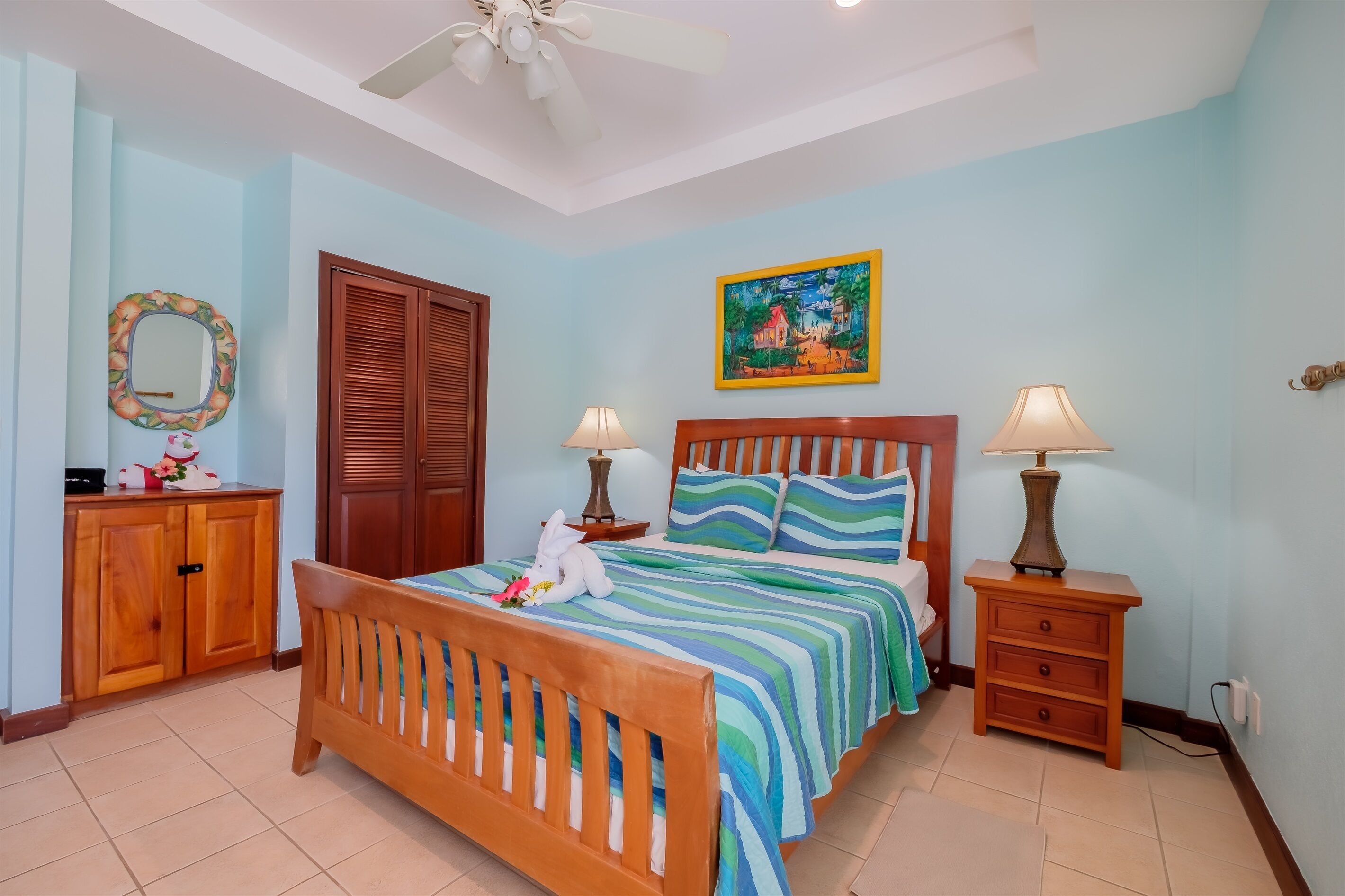A bedroom with a wooden bed, two bedside tables with lamps, a wardrobe, a mirror, and a painting on the wall.