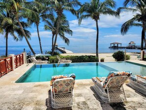 A pool with lounge chairs, palm trees, and a view of the ocean.