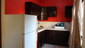 A compact kitchen with dark wooden cabinets, a white refrigerator, and a stove. - Bungalows Yessy Tetos (Rincón de Guayabitos)