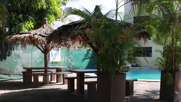 An outdoor seating area with wooden tables and benches, surrounded by potted plants and a pool. - Bungalows Yessy Tetos (Rincón de Guayabitos)