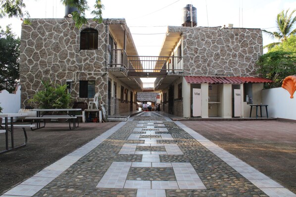 A courtyard with stone buildings, outdoor seating, and a tiled walkway. - Bungalows Yessy Tetos (Rincón de Guayabitos)