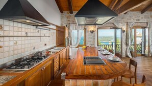 A kitchen with a central island, wooden cabinets, and a stone wall. - Stunning stone house nestled in the heart of the historic old town of Vrsar. (Vrsar)