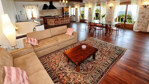 A spacious living area with a sofa, coffee table, and patterned rug. A kitchen with a stove and dining area is visible in the background. - Stunning stone house nestled in the heart of the historic old town of Vrsar. (Vrsar)