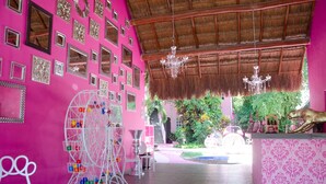 Un intérieur dynamique, avec un mur rose, de nombreux miroirs, un carrousel en métal blanc et un toit de chaume.