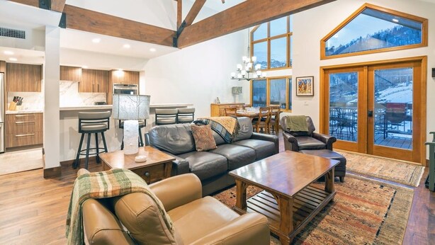 A spacious living area with a high ceiling, a dining area, and a view of a snowy landscape through large windows. - Kayenta II 16 3 Bedroom/3 Bathroom Slopeside (Mountain Village)