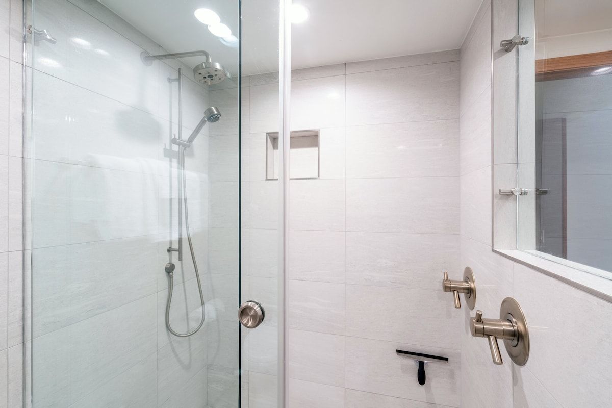 A modern bathroom with a glass shower enclosure, a wall-mounted faucet, and a mirror.