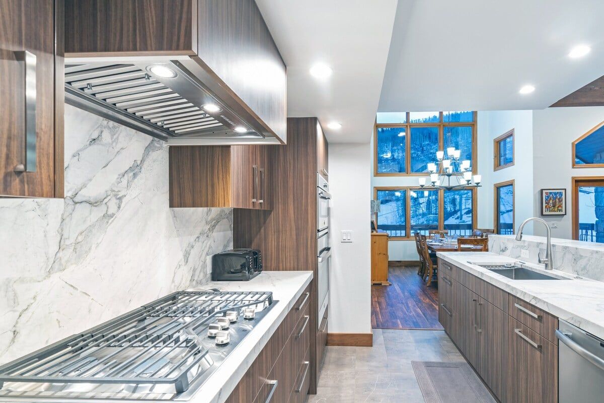 Una cocina moderna con estufa a gas, armarios de madera y vistas a un comedor a través de amplios ventanales.