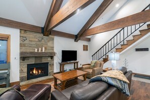 A living room with a stone fireplace, leather sofa, wooden coffee table, and a staircase with a black railing.