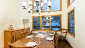 A dining room with a wooden table set for six, large windows, and a chandelier.