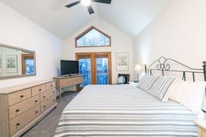 A bedroom with a bed, dresser, television, and a window with a view.