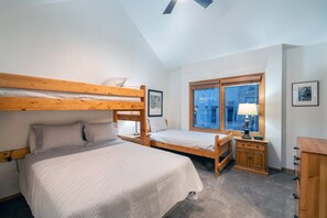 A room with bunk beds, a window with a view, a desk with a lamp, and a cabinet.