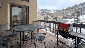 A deck with a round table and chairs, a grill, and a view of a snowy mountain range. - Kayenta II 16 3 Bedroom/3 Bathroom Slopeside (Mountain Village)