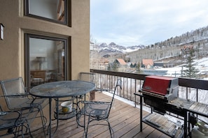 Une terrasse avec une table ronde et des chaises, un barbecue et une vue sur une chaîne de montagnes enneigées.