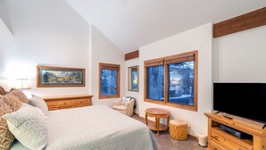 A bedroom with a large bed, a television, a small round table, and a window with a view of trees. - Kayenta II 16 3 Bedroom/3 Bathroom Slopeside (Mountain Village)