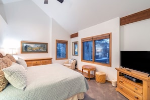 Une chambre à coucher avec un grand lit, une télévision, une petite table ronde et une fenêtre donnant sur des arbres.
