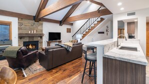 A modern living room with a fireplace, a sofa, a TV, and a staircase leading to a kitchen area.
