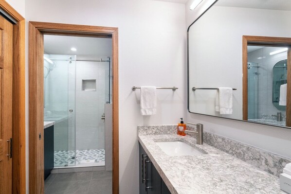 A modern bathroom with a glass shower enclosure, a marble sink, and a large mirror.