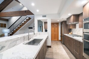 A modern kitchen with marble countertops, wooden cabinets, stainless steel appliances, and a staircase leading to another level. - Kayenta II 16 3 Bedroom/3 Bathroom Slopeside (Mountain Village)