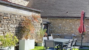 Un espace patio agrémenté d’un mur en pierre, d’une table avec des chaises et d’un parasol rouge.