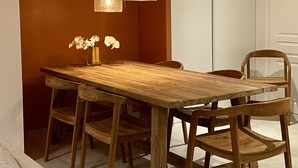 Une table à manger en bois avec des chaises, un vase rempli de fleurs et des luminaires suspendus.