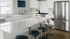 Una cocina moderna con armarios blancos, un refrigerador de acero inoxidable, una isla grande con taburetes de bar y una lámpara colgante de diseño geométrico.