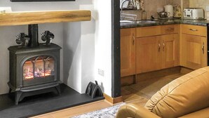 A living room with a fireplace, a sofa, and a kitchen area with wooden cabinets and a countertop. - 2 bedroom accommodation in Ambleside (Ambleside)