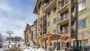 A multi-story hotel with balconies, a stone fire pit, and a ski lift in the background.