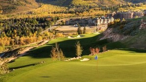 A golf course with a clubhouse, surrounded by autumn-colored trees and hills.