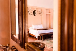 A bedroom with a bed, a bench, a wall-mounted light fixture, and a mirror. - Riad Mellado by Grupo Afekto (Guanajuato)