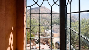 A room with a large window offering a view of a mountainous landscape and a courtyard with outdoor furniture and plants. - Riad Mellado by Grupo Afekto (Guanajuato)