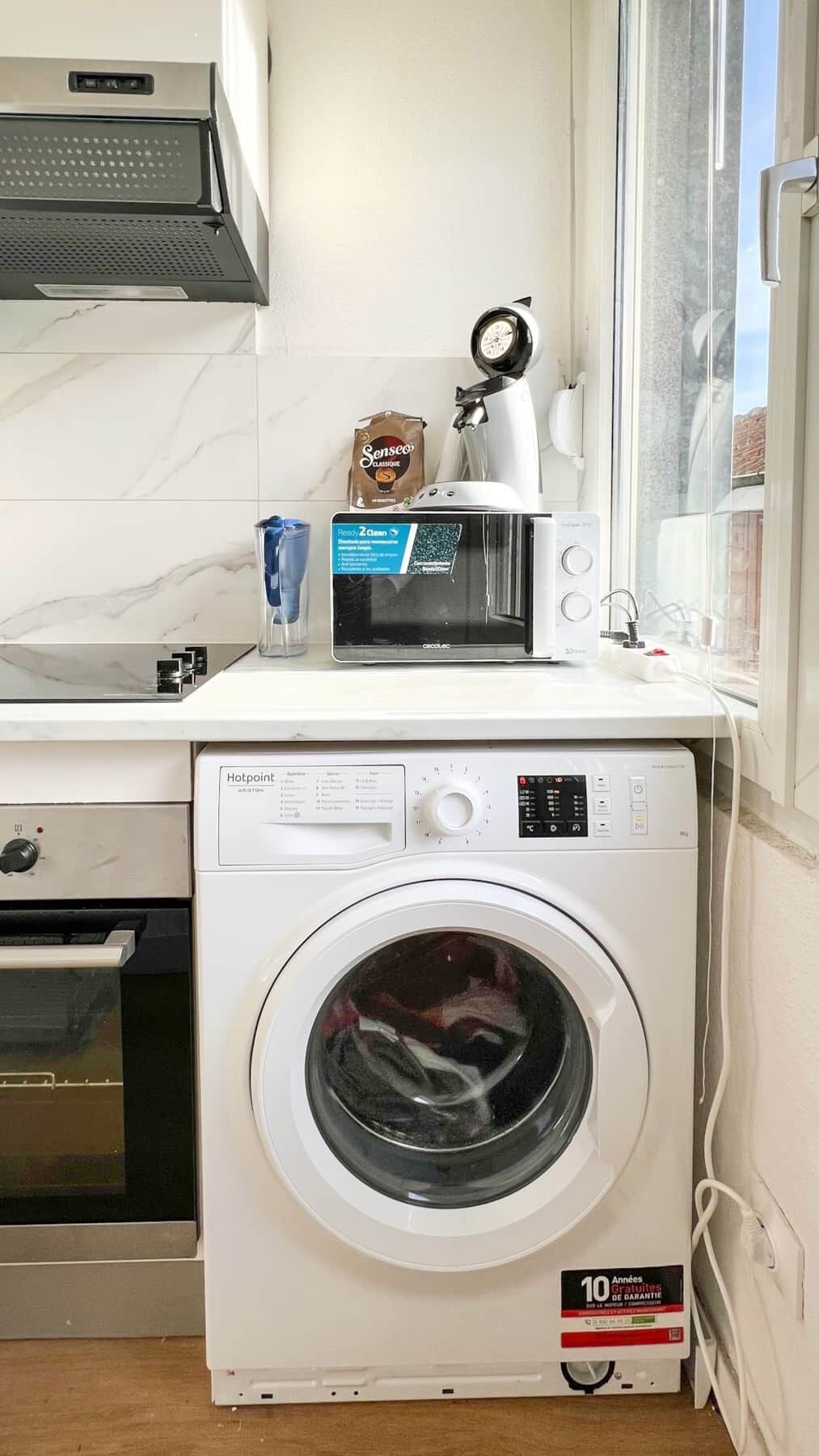 Eine kompakte Küche mit Waschmaschine, Mikrowelle und Kaffeemaschine.