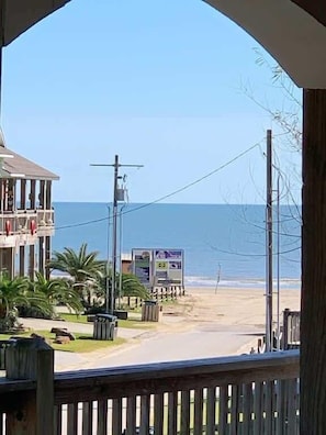 A beach view with a building, palm trees, and a signboard.