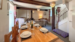 Un'area pranzo con un tavolo di legno apparecchiato per quattro persone, un divano, una lampada e una scala.
