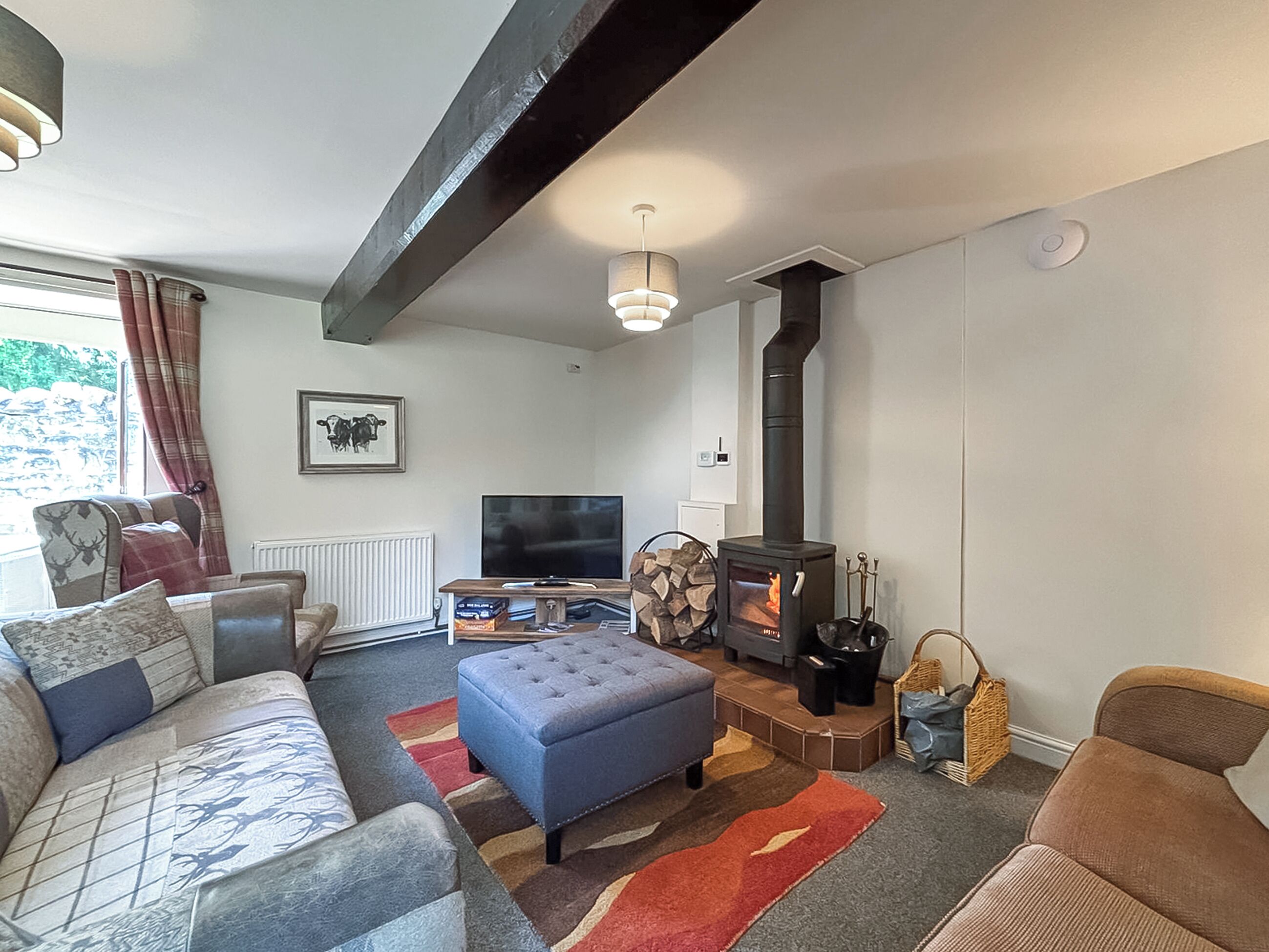 A living room with a sofa, ottoman, TV, fireplace, and a window with curtains.