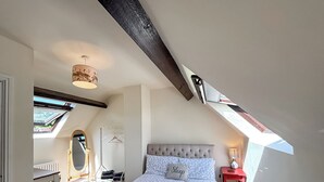Una camera da letto con soffitto spiovente, un letto con copripiumino decorato, un comodino con lampada e una finestra vista.