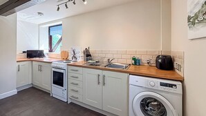 Una cucina compatta con mobili bianchi, forno a incasso, microonde, lavandino e lavatrice.