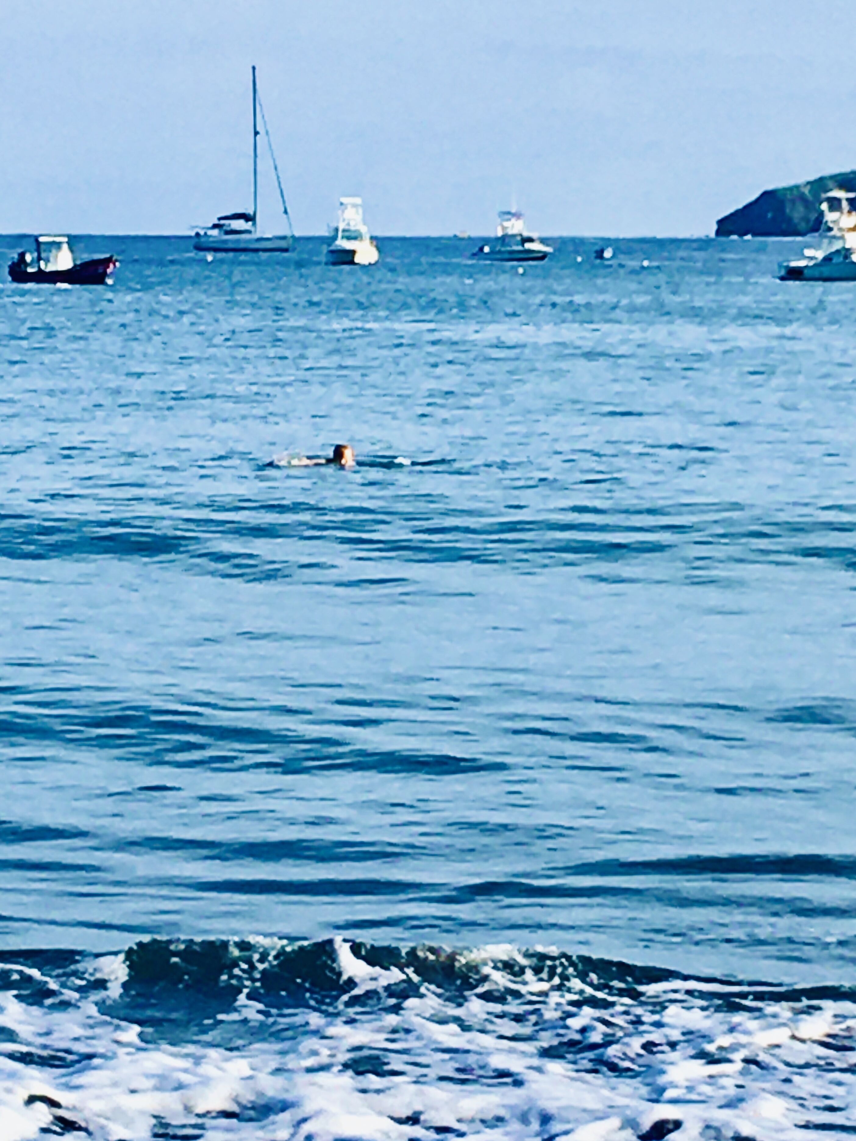 Eine Küstenansicht mit Booten und einer Person, die im Wasser schwimmt.