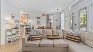 Un salon avec un canapé d’angle beige, une table basse en bois et un coin repas comprenant une table et des chaises en bois.