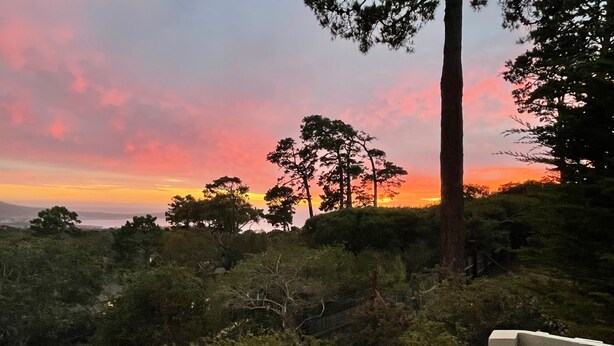 A sunset view from a balcony with a wooden railing and a bench.