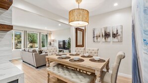 A spacious living room with a wooden dining table, comfortable seating, and a large window offering a view of greenery. - Modern Beach House Oasis w/ Private Patio (san diego)